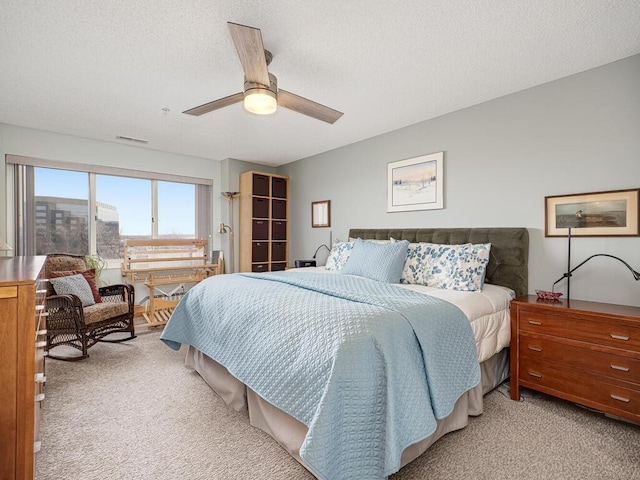 bedroom featuring ceiling fan, light colored carpet, and a textured ceiling