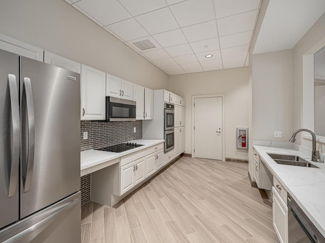 kitchen with sink, appliances with stainless steel finishes, white cabinetry, tasteful backsplash, and light stone countertops