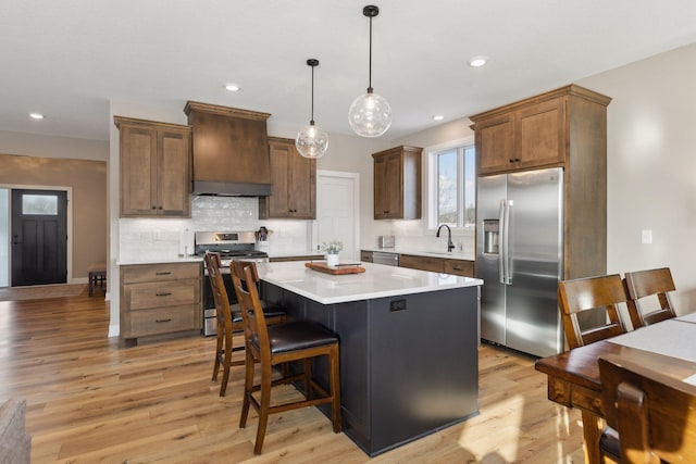 kitchen with appliances with stainless steel finishes, a center island, premium range hood, hanging light fixtures, and sink