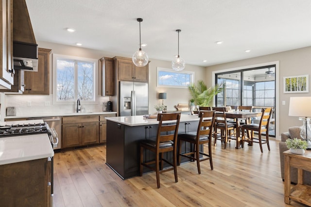 kitchen featuring hanging light fixtures, sink, stainless steel fridge with ice dispenser, a center island, and light hardwood / wood-style floors