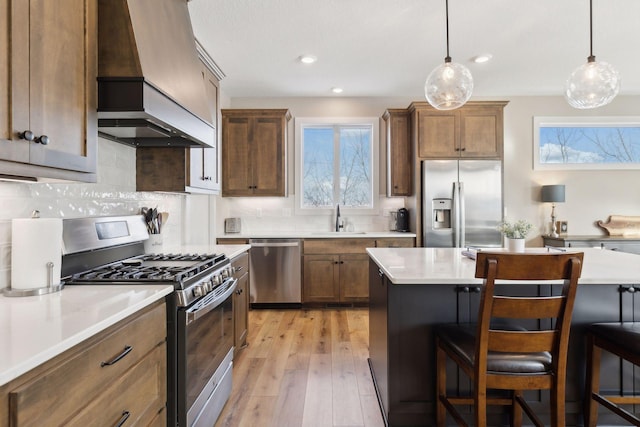 kitchen with appliances with stainless steel finishes, custom range hood, hanging light fixtures, sink, and a breakfast bar area