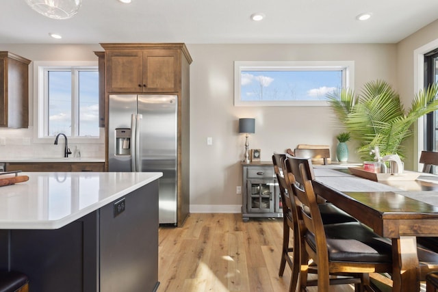 kitchen featuring stainless steel refrigerator with ice dispenser, sink, backsplash, and light wood-type flooring