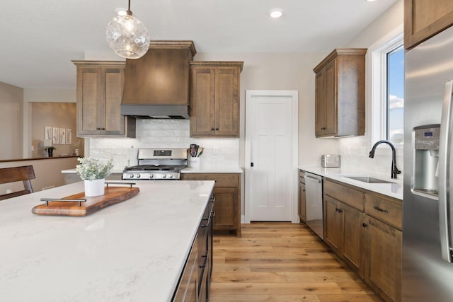 kitchen with custom exhaust hood, light hardwood / wood-style floors, sink, decorative light fixtures, and stainless steel appliances