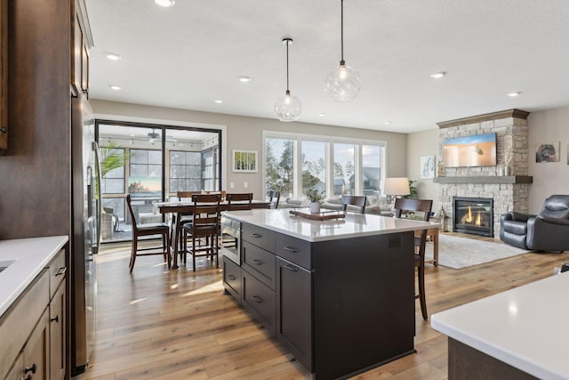 kitchen with light wood-type flooring, decorative light fixtures, a center island, and a fireplace