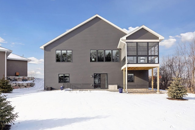 snow covered rear of property featuring a sunroom