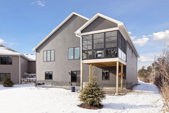 snow covered back of property featuring a sunroom