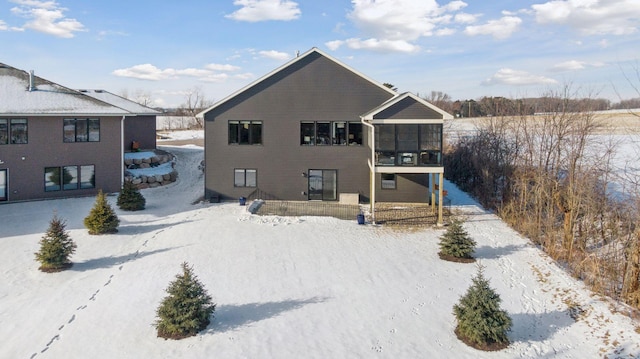 snow covered back of property featuring a sunroom