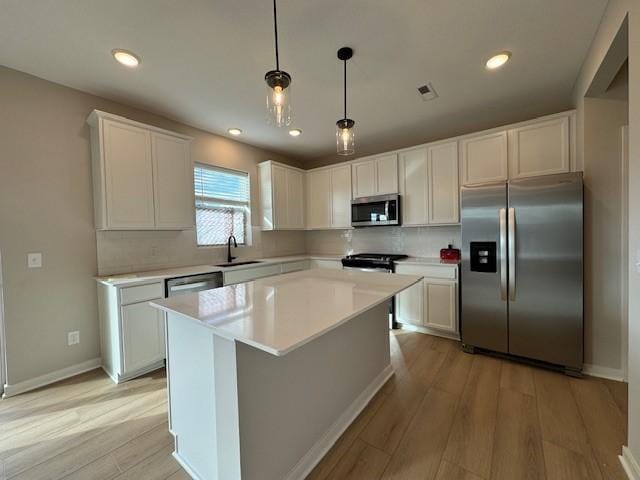 kitchen with stainless steel appliances, decorative light fixtures, white cabinetry, and a center island