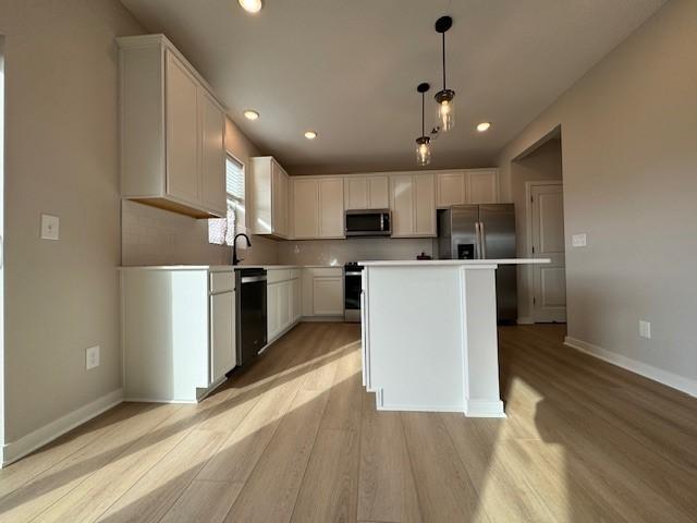 kitchen featuring stainless steel appliances, light wood-type flooring, a kitchen island, white cabinetry, and decorative light fixtures