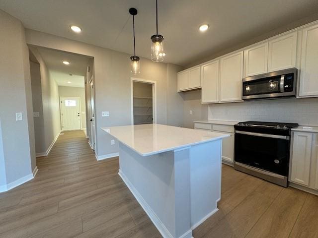 kitchen with white cabinets, light hardwood / wood-style flooring, a kitchen island, pendant lighting, and appliances with stainless steel finishes