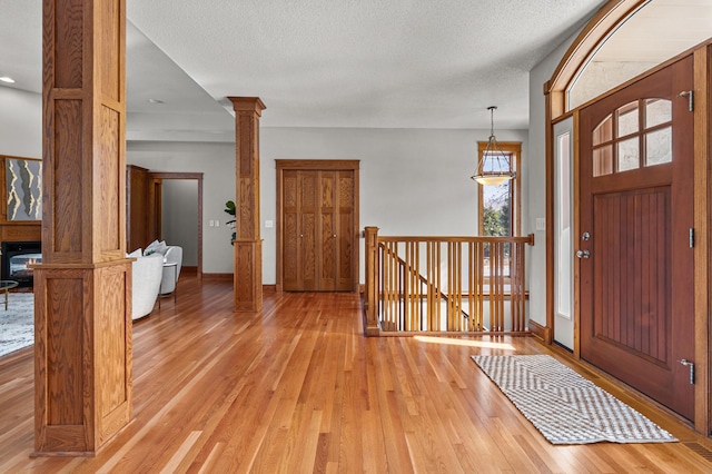 entrance foyer featuring light wood finished floors, baseboards, a textured ceiling, and ornate columns