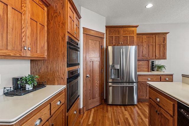 kitchen featuring brown cabinets, black appliances, a textured ceiling, light wood finished floors, and light countertops