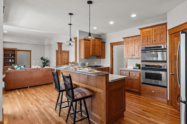 kitchen featuring light wood finished floors, open floor plan, a breakfast bar area, appliances with stainless steel finishes, and a peninsula