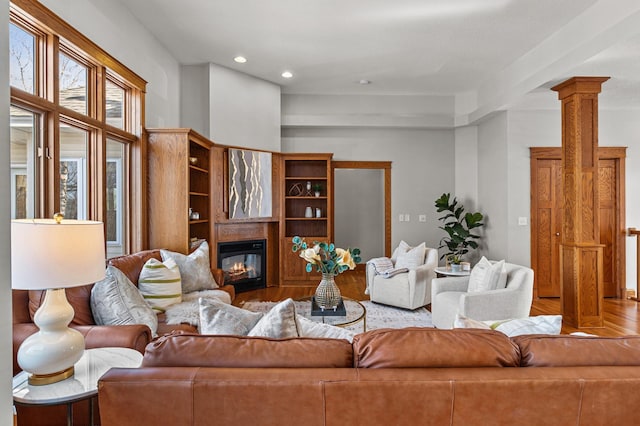 living area featuring a glass covered fireplace, recessed lighting, wood finished floors, and ornate columns