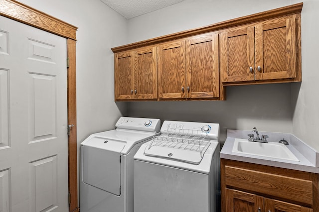 clothes washing area with a sink, cabinet space, a textured ceiling, and washing machine and dryer