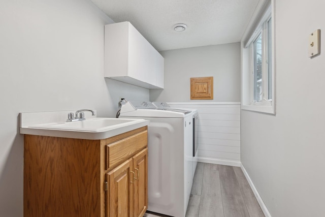 clothes washing area with light hardwood / wood-style floors, a textured ceiling, sink, separate washer and dryer, and cabinets