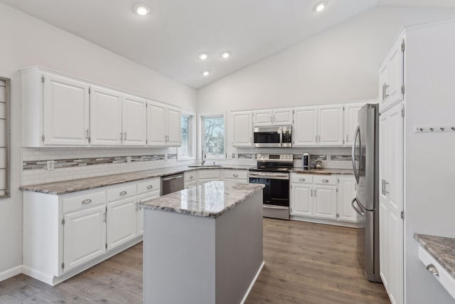 kitchen featuring appliances with stainless steel finishes, a center island, white cabinetry, sink, and light stone counters