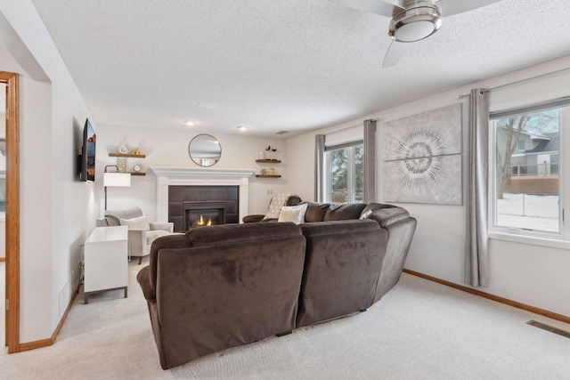 carpeted living room featuring ceiling fan, a textured ceiling, and a tiled fireplace