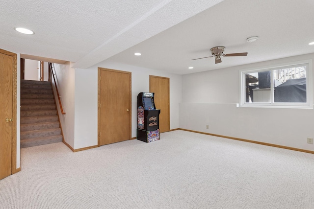 basement with ceiling fan, light colored carpet, and a textured ceiling