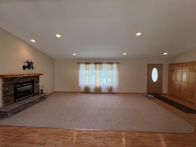 living room with vaulted ceiling, wood-type flooring, and a stone fireplace