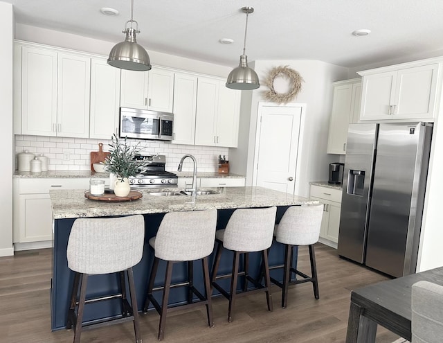 kitchen featuring dark hardwood / wood-style floors, appliances with stainless steel finishes, white cabinetry, and an island with sink