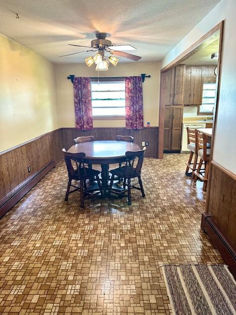 dining area with ceiling fan, a baseboard heating unit, a textured ceiling, and wood walls