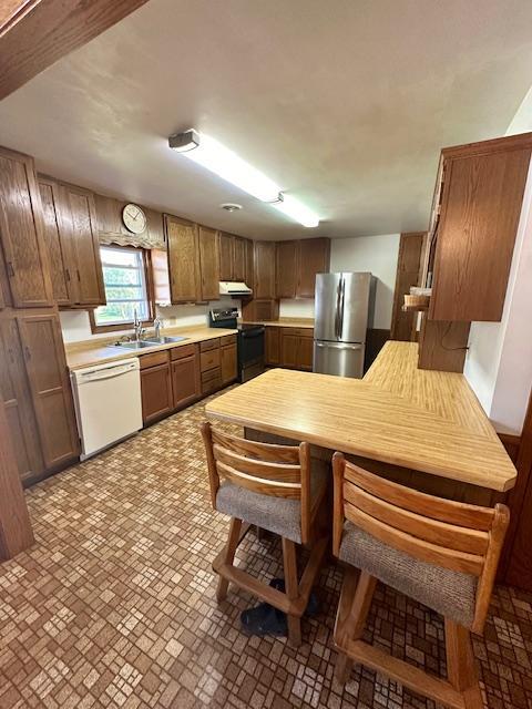 kitchen with sink, stainless steel refrigerator, white dishwasher, kitchen peninsula, and electric stove