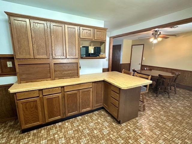 kitchen with ceiling fan, a breakfast bar area, wooden walls, and kitchen peninsula