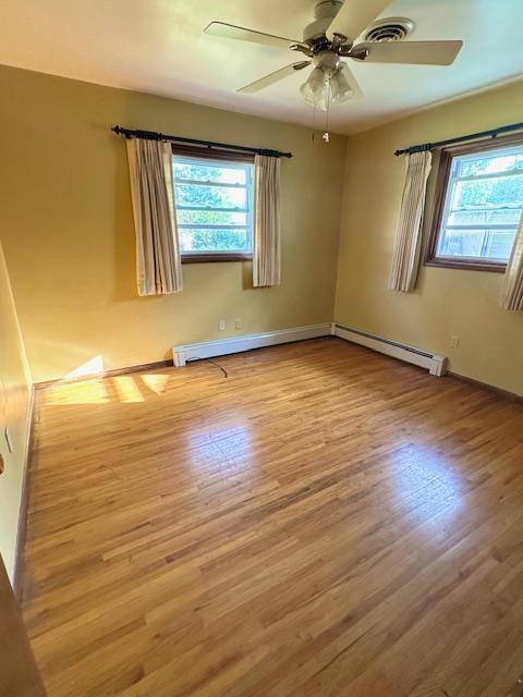 empty room featuring a baseboard heating unit, plenty of natural light, light hardwood / wood-style floors, and ceiling fan