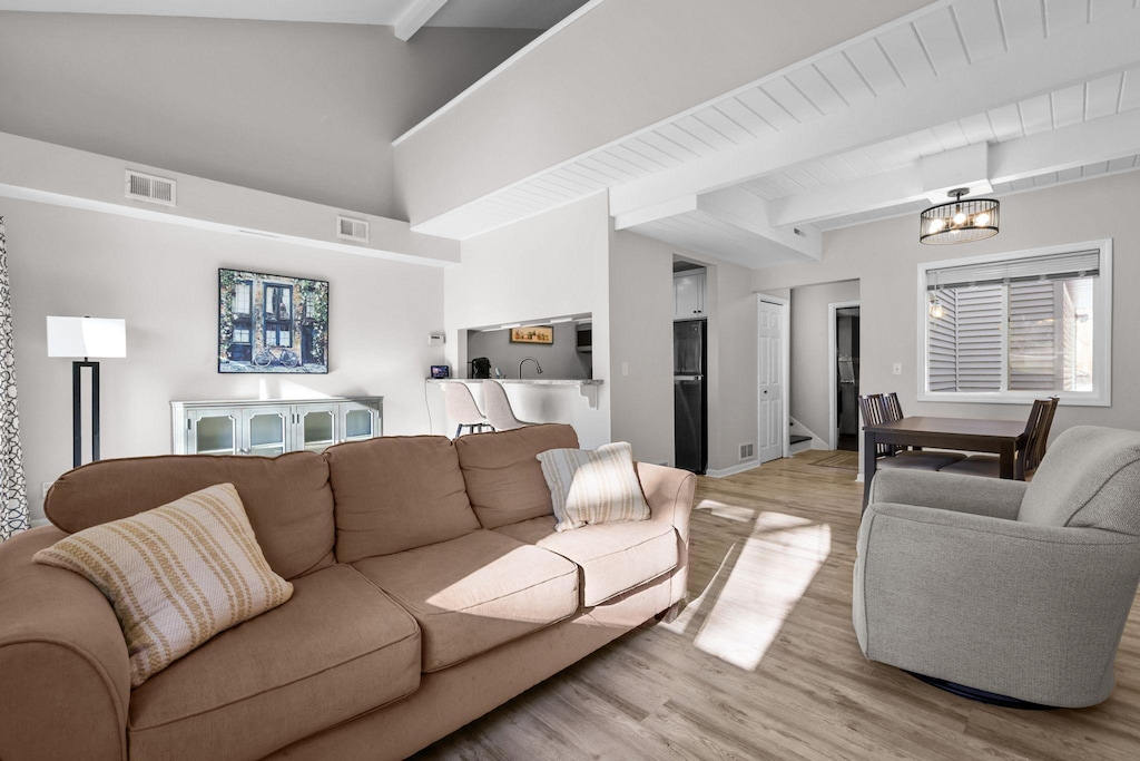 living room with light wood-type flooring, a notable chandelier, and beam ceiling