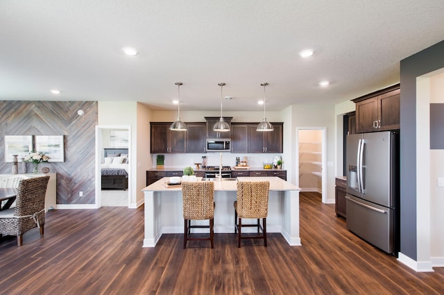 kitchen with a center island with sink, appliances with stainless steel finishes, dark brown cabinets, and hanging light fixtures