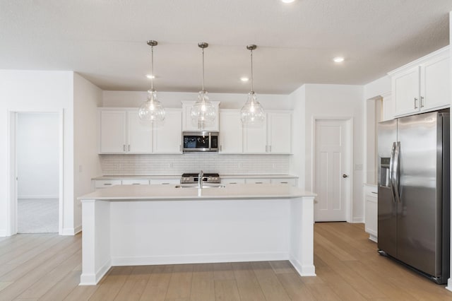 kitchen with white cabinetry, a center island with sink, stainless steel appliances, sink, and pendant lighting