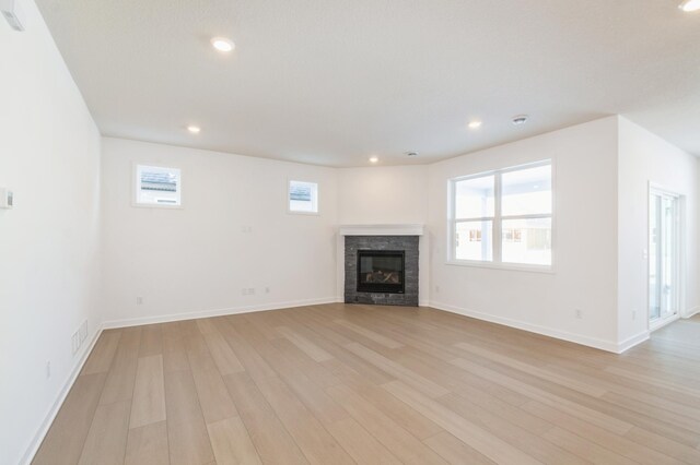 unfurnished living room featuring a fireplace, light wood-type flooring, and a healthy amount of sunlight