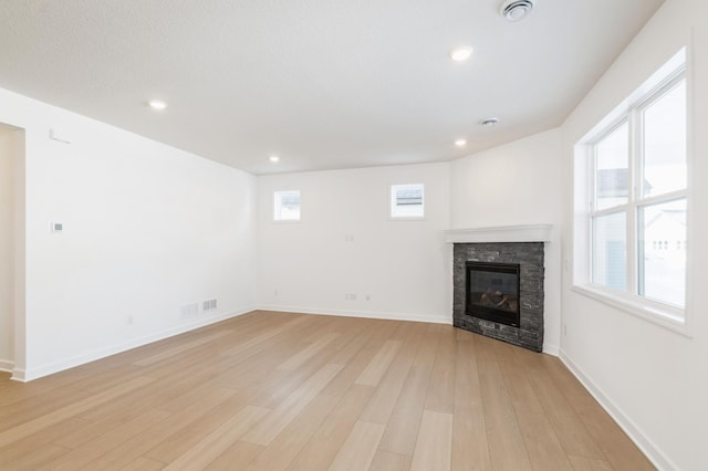 unfurnished living room with light wood-type flooring, a healthy amount of sunlight, and a stone fireplace