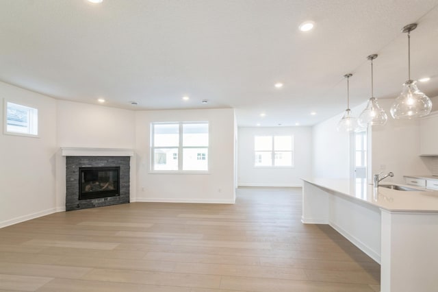 unfurnished living room with a fireplace, sink, and light wood-type flooring