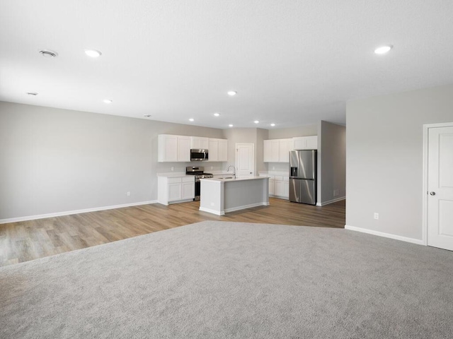 kitchen with light carpet, appliances with stainless steel finishes, a kitchen island with sink, white cabinets, and sink