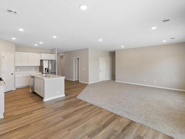 kitchen featuring appliances with stainless steel finishes, white cabinetry, light hardwood / wood-style floors, sink, and a center island with sink