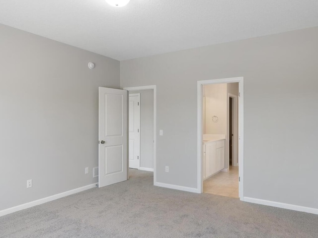 unfurnished bedroom featuring light colored carpet and ensuite bath