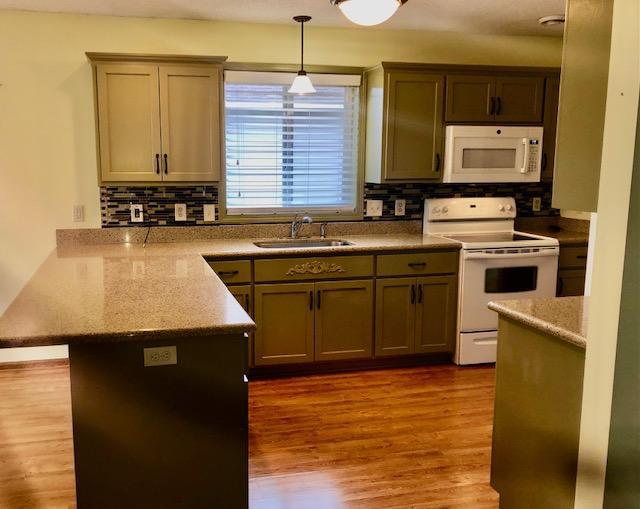 kitchen with pendant lighting, sink, light stone counters, and white appliances