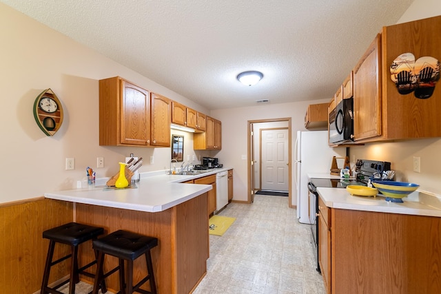 kitchen featuring a breakfast bar area, light floors, a peninsula, black appliances, and a sink