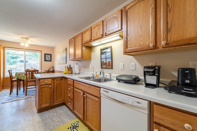 kitchen featuring brown cabinetry, dishwasher, a peninsula, light countertops, and a sink