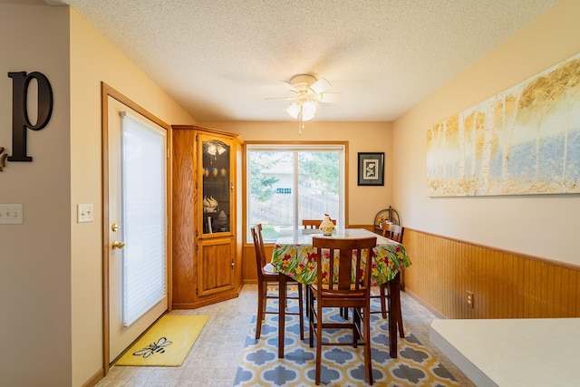 dining room with a wainscoted wall, ceiling fan, a textured ceiling, and wooden walls