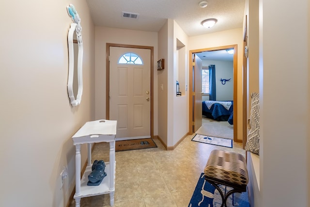 foyer entrance with visible vents, a textured ceiling, and baseboards