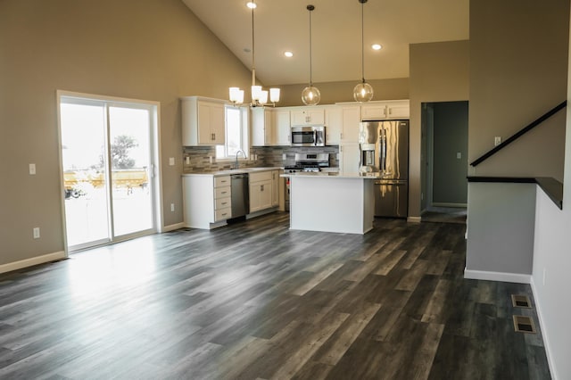 kitchen featuring stainless steel appliances, decorative light fixtures, white cabinetry, a center island, and high vaulted ceiling