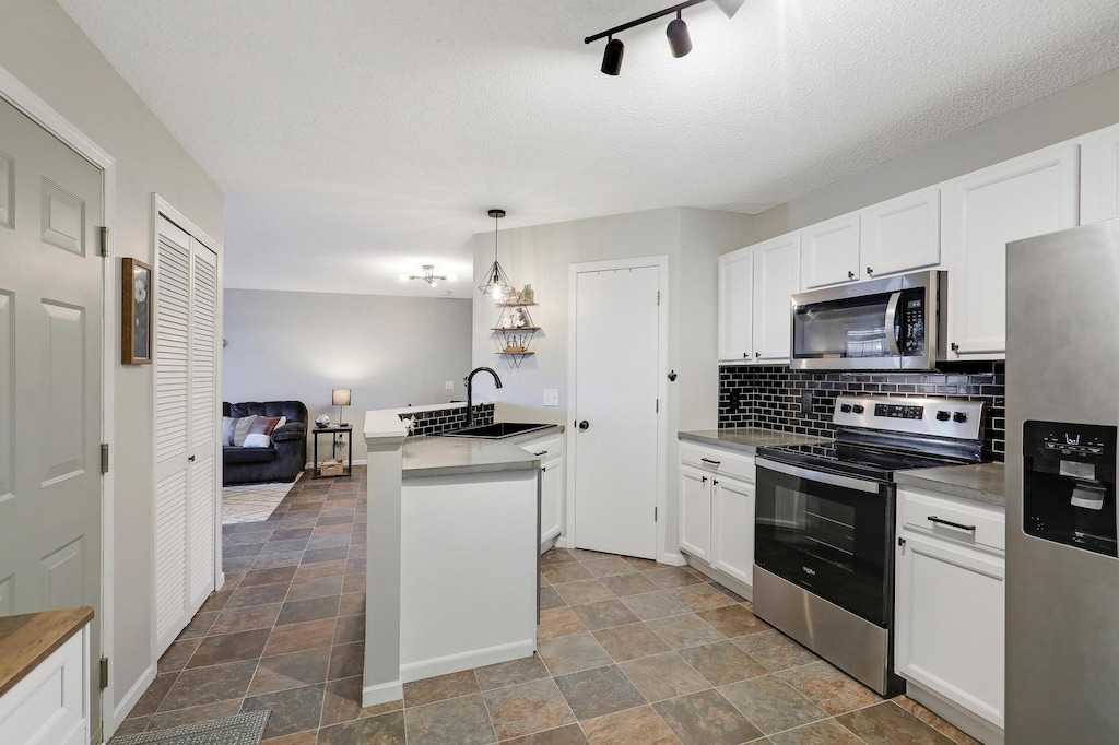 kitchen featuring sink, white cabinets, hanging light fixtures, and appliances with stainless steel finishes