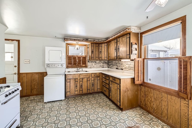 kitchen with white range with gas cooktop, brown cabinetry, light countertops, stacked washing maching and dryer, and a sink