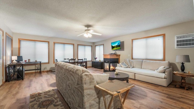 living room with a textured ceiling, ceiling fan, wood finished floors, a multi sided fireplace, and a wall mounted air conditioner