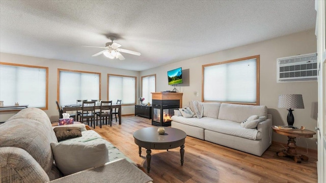 living area with light wood finished floors, a wall mounted AC, a ceiling fan, a textured ceiling, and a multi sided fireplace