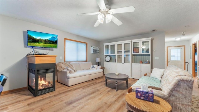 living room with a textured ceiling, a multi sided fireplace, a ceiling fan, and light wood-style floors