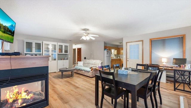 dining space featuring ceiling fan, light wood-style flooring, and a multi sided fireplace